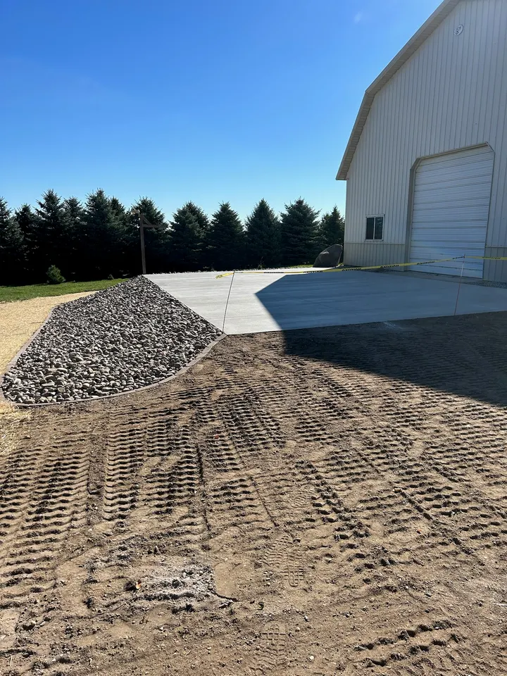 Compacted gravel base graded flat beside a white metal building, with a gravel pile in the foreground