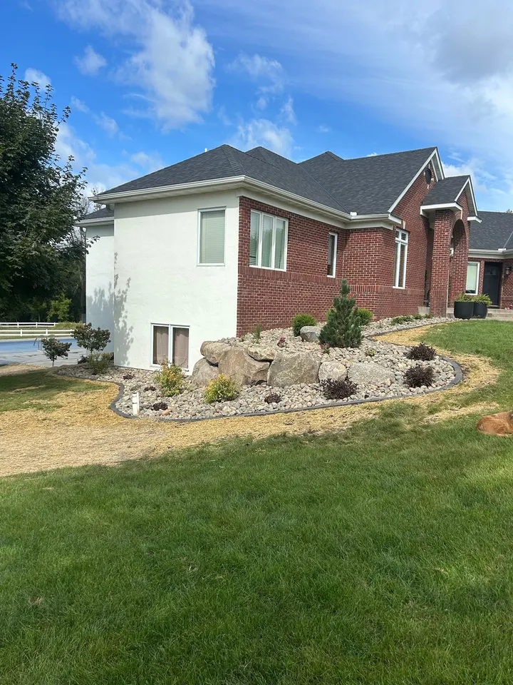 River rock landscaping beds with boulders and young shrubs along the side of a brick home
